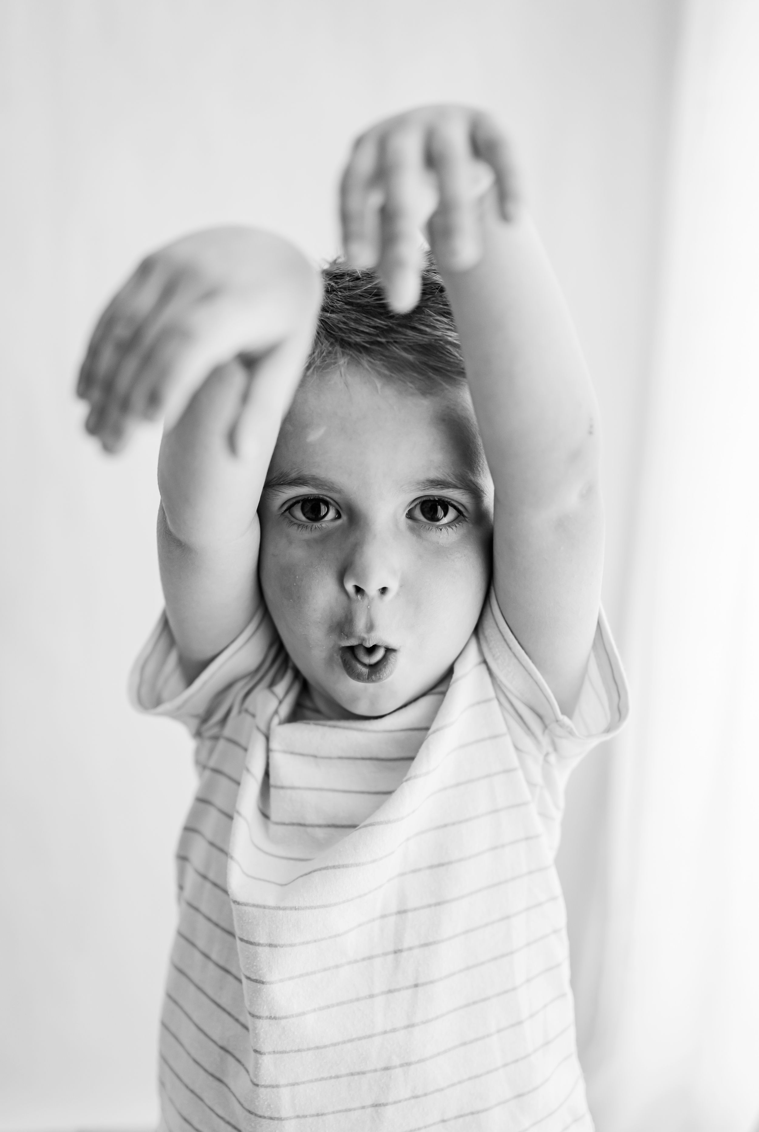 Black and white portrait of a playful child with raised hands making a silly expression.
