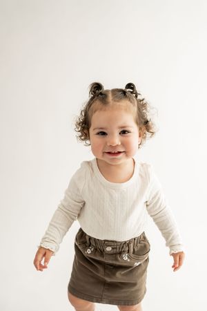 A toddler wearing a white sweater and brown skirt dances and twirls in a four-panel progression shot.