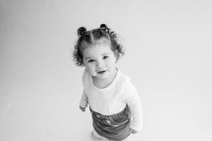 Adorable toddler in white shirt wearing a funny expression while looking up at the camera.