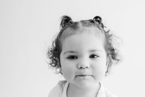 Three close-up photos of a baby with curly hair showing different expressions on a white background.