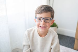 Person wearing glasses and cream colored sweater sitting indoors.