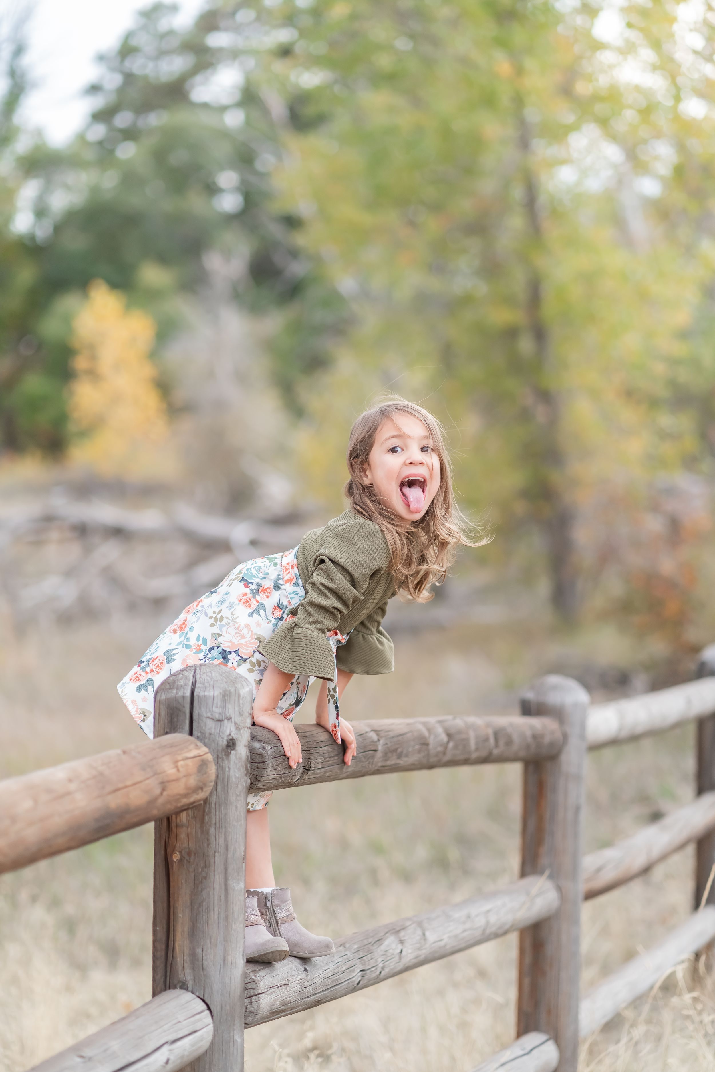 Playful child balancing on wooden fence rail in outdoor nature setting.