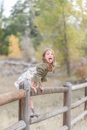 Playful child balancing on wooden fence rail in outdoor nature setting.