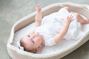 Baby in white outfit lying peacefully on soft gray cushioned surface.