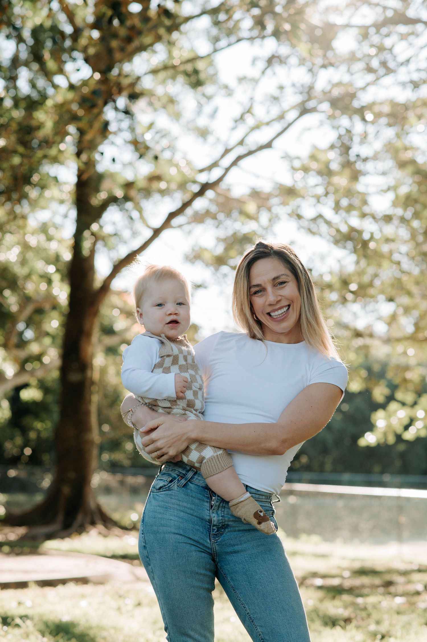 Joyful outdoor portrait of parent and baby laughing together in a sunny park setting.