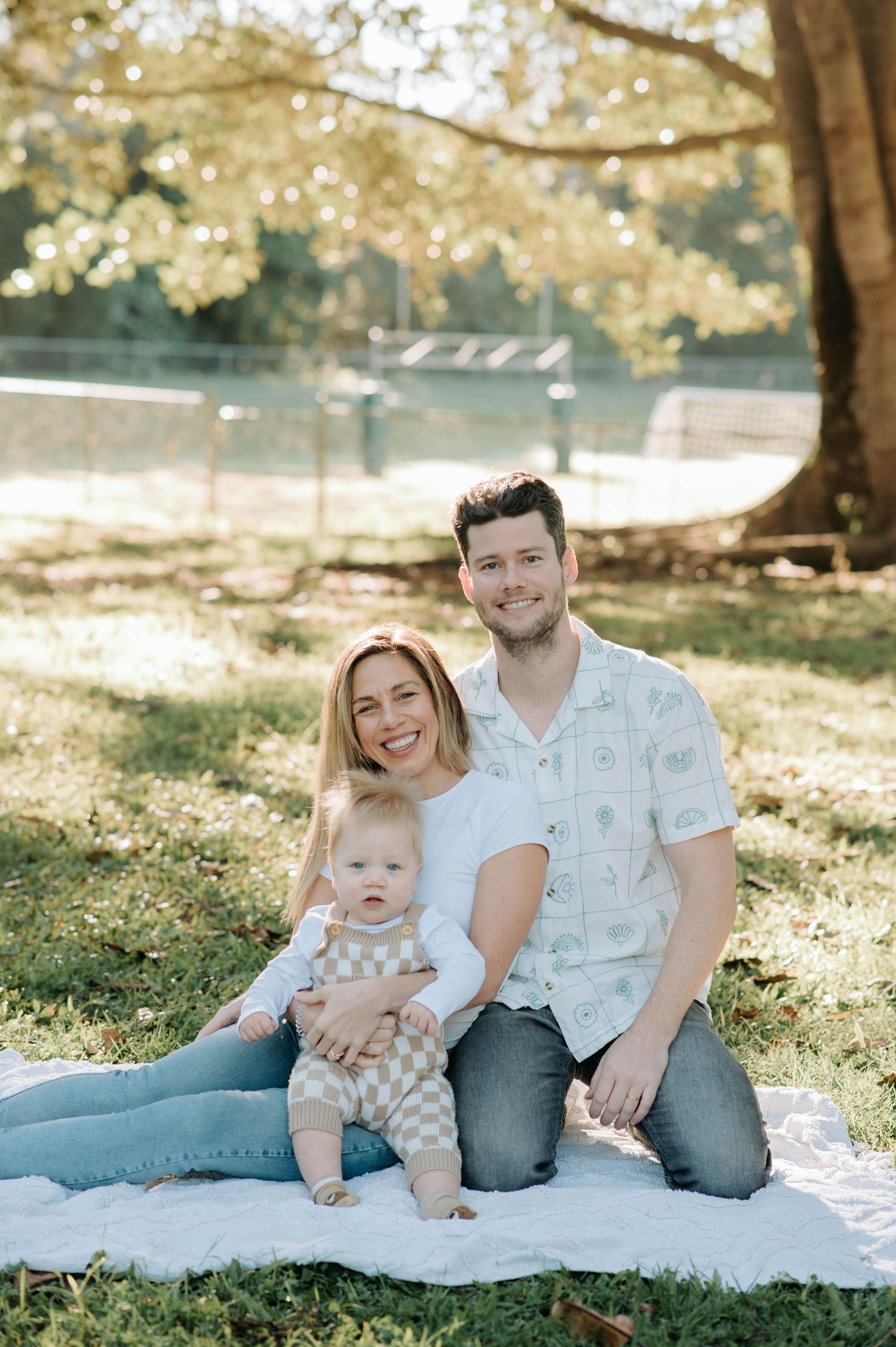 Family sits together on blanket during outdoor photoshoot in golden afternoon light.