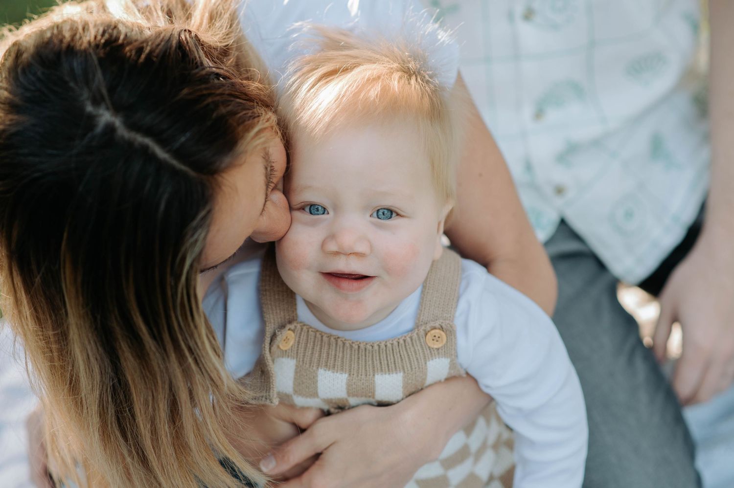 Intimate family moment captured as parent gives baby a loving kiss outdoors.