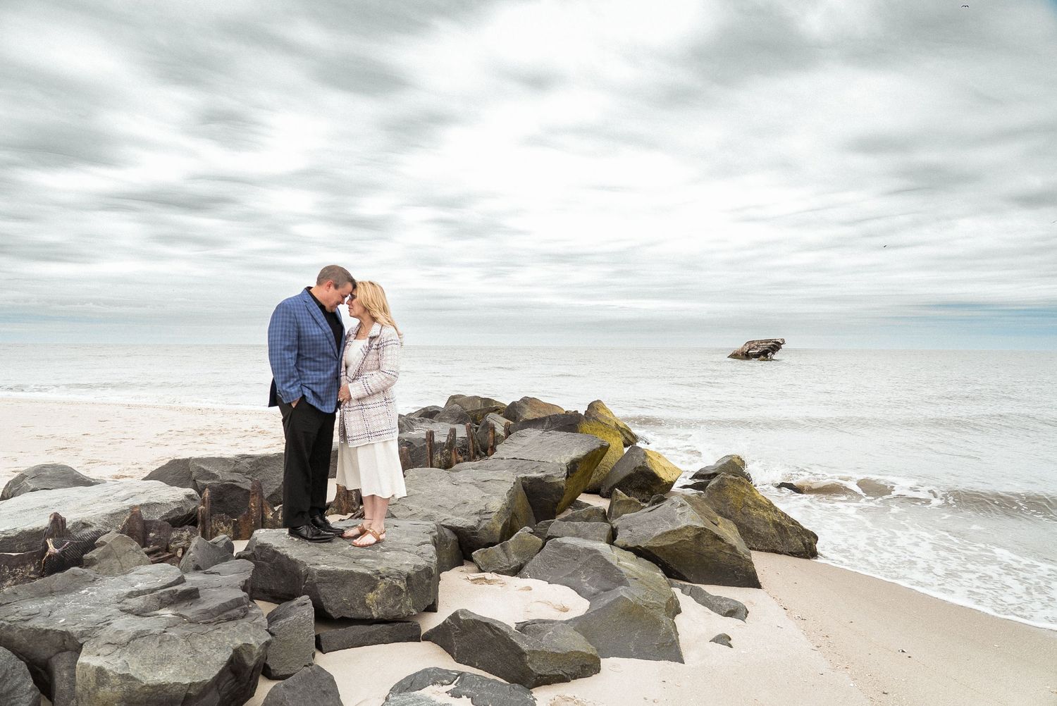 Couple sharing intimate moment on rocky beach during overcast day.