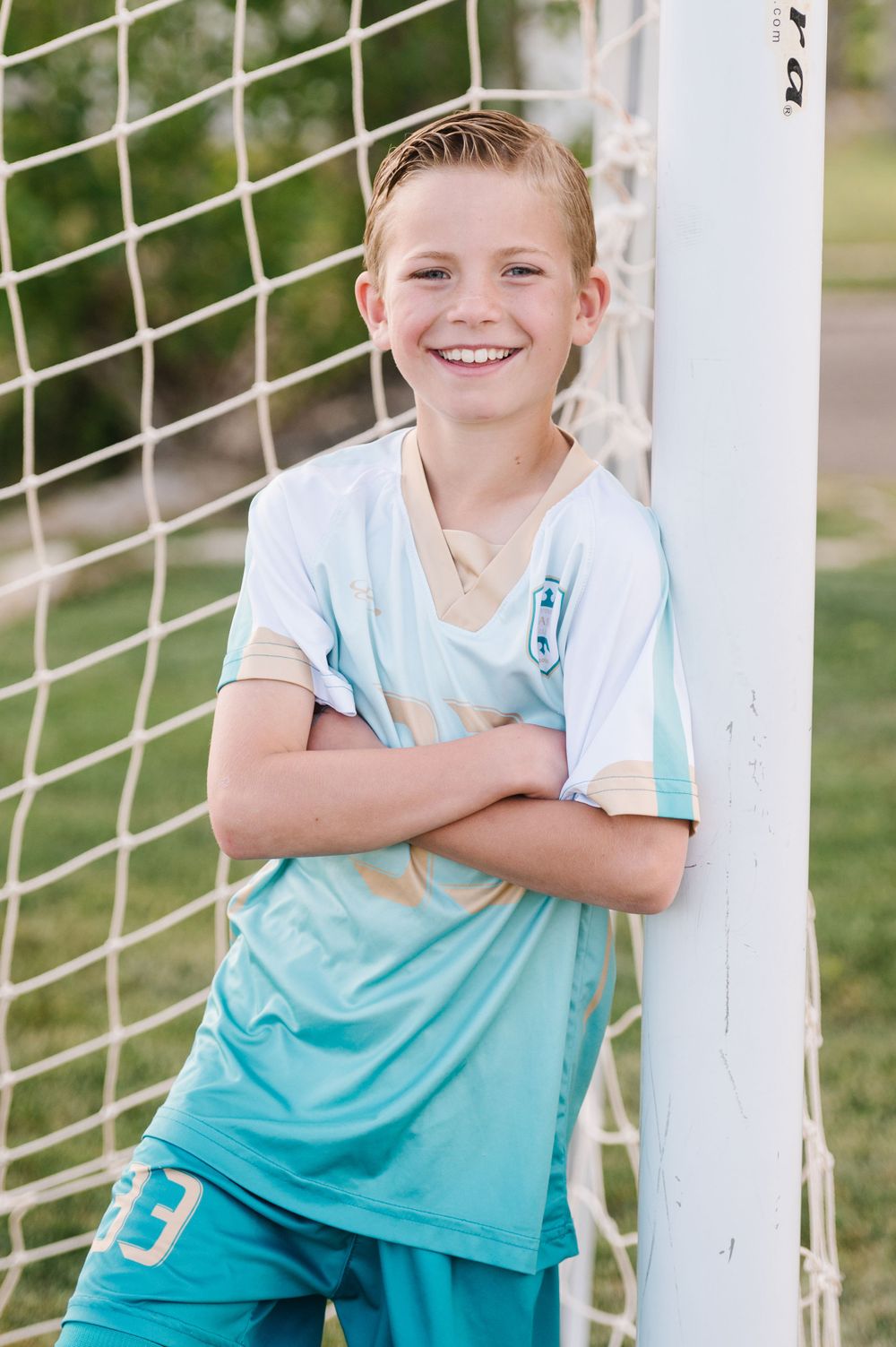 Young athlete in turquoise soccer uniform poses confidently by a goal post.
