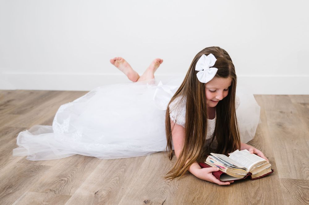 Person in white dress lying on wooden floor reading book.