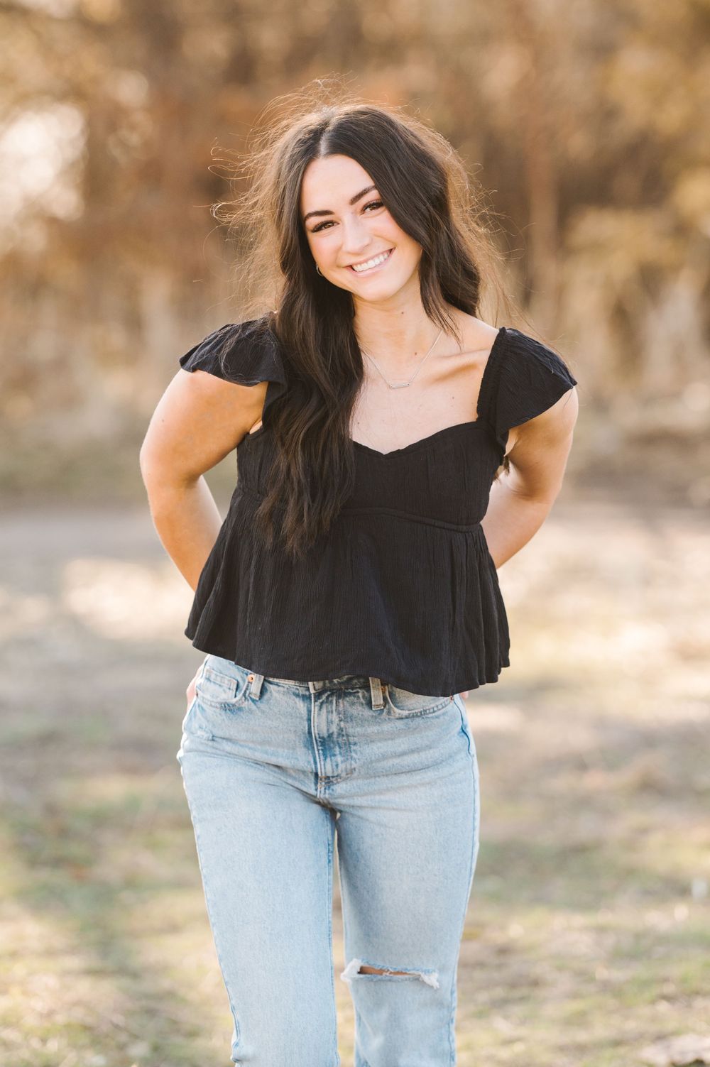 An outdoor portrait in a black peplum top and distressed jeans against a natural background.