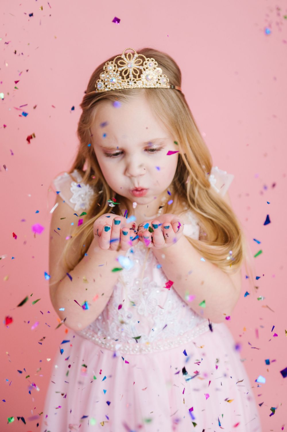 A magical princess moment with confetti, tiara and pink dress against a pink background.