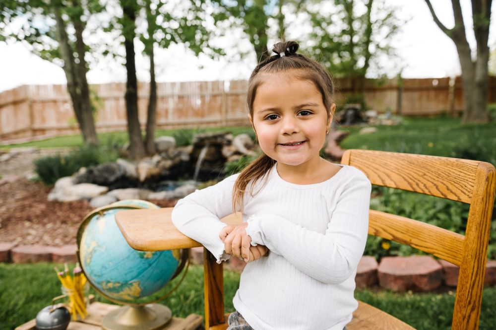 Young student with braids smiles while studying globe in outdoor garden setting.