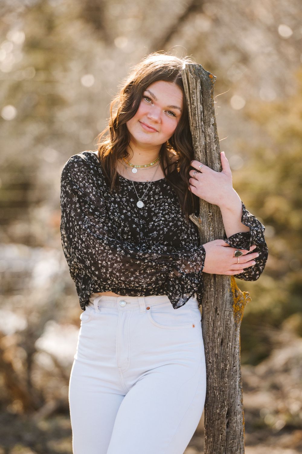 A springtime outdoor portrait with a floral top and white pants against a sunlit natural background.