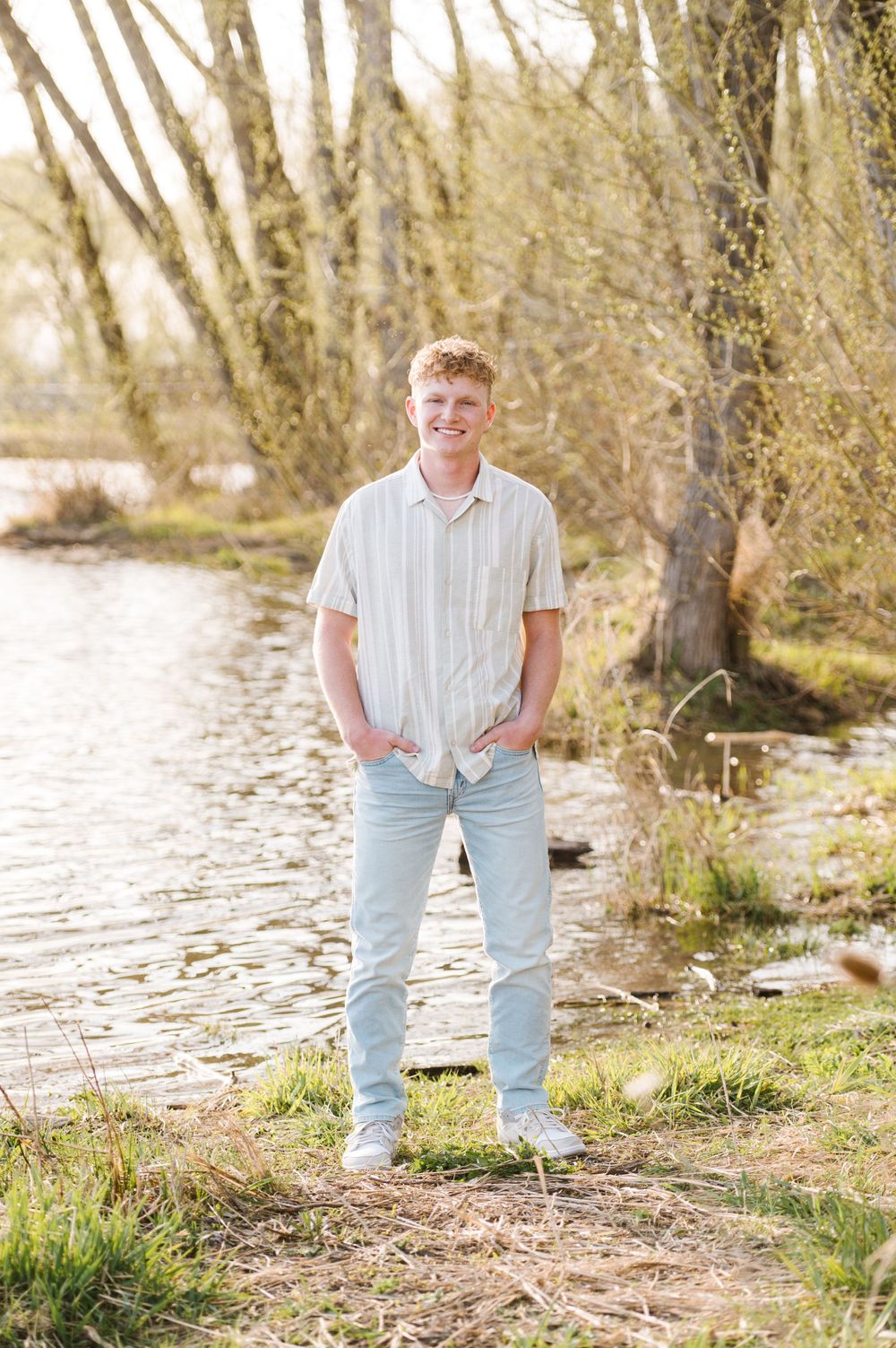 Casual portrait by riverside wearing light colored shirt and jeans.