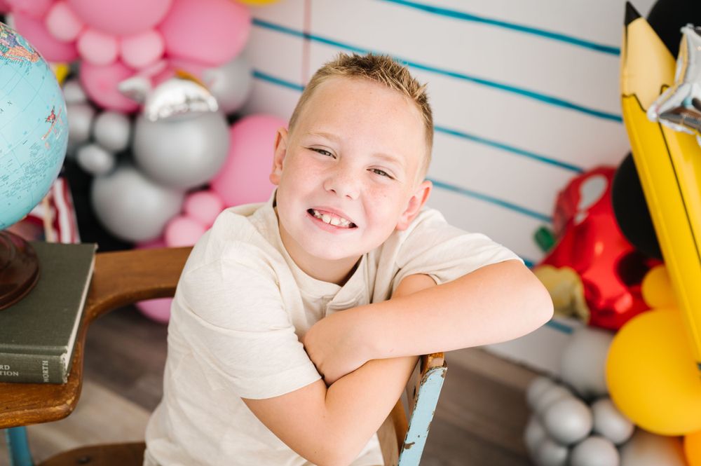 A student smiles at the camera against a backdrop of school-themed balloons and decorations.