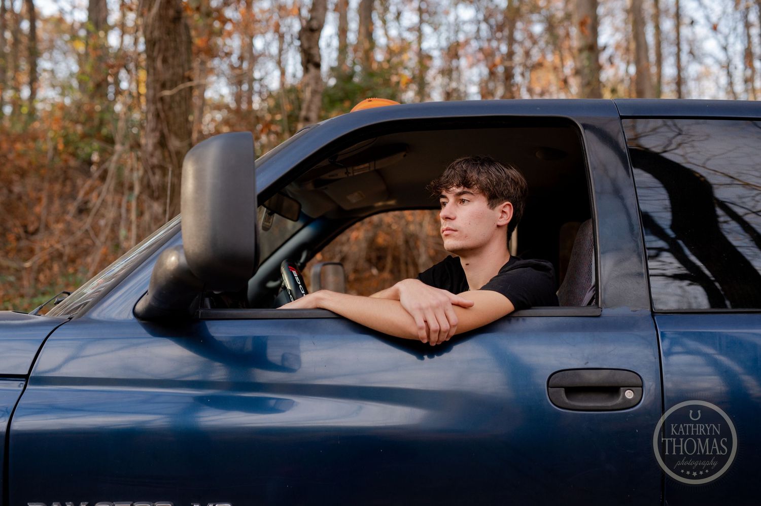 Person leaning out window of parked Ram pickup truck on autumn day.