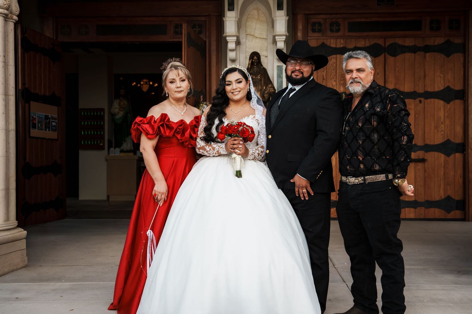 A quinceañera in a white ball gown poses with three guests, including a woman in red, at an elegant venue.