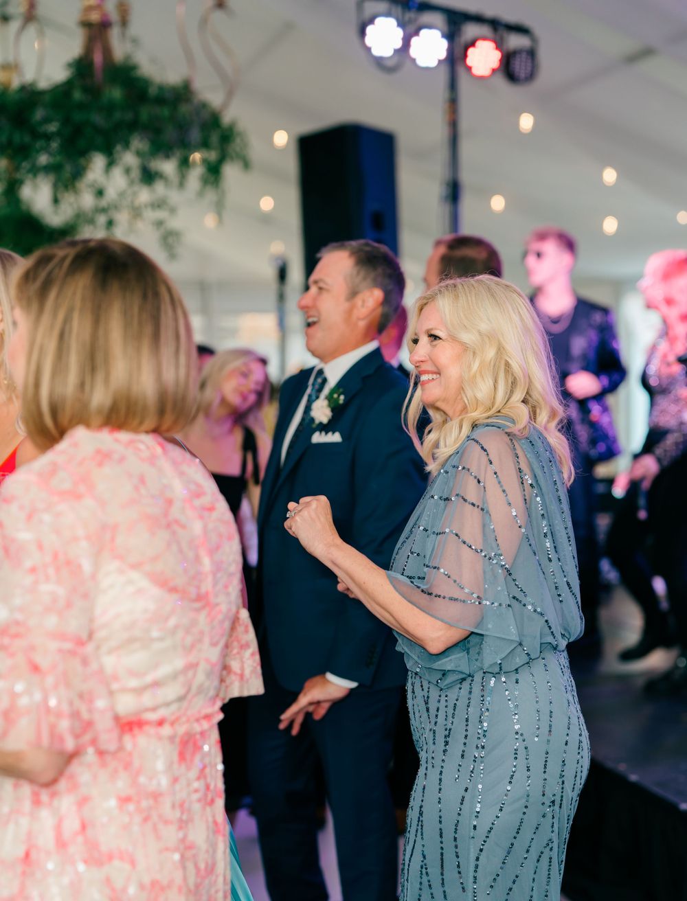 Wedding guests dancing and enjoying themselves at an indoor reception with stage lighting and decorations.