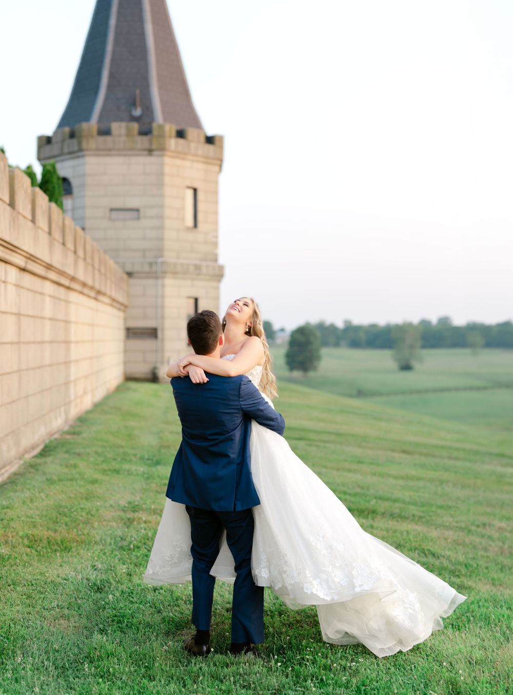 A wedding couple shares an intimate moment near a castle tower with sweeping grounds in the background.