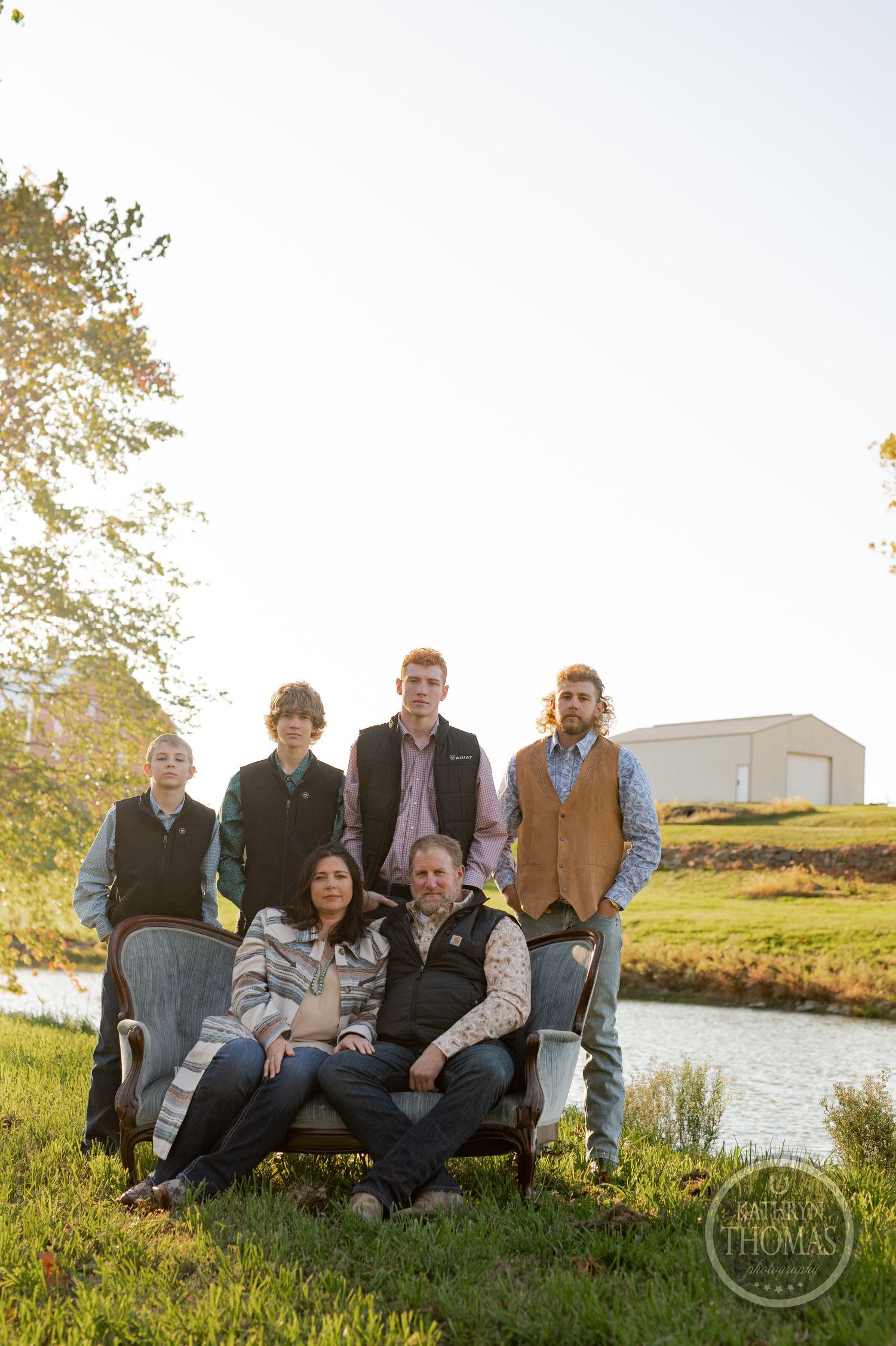 Group photo of family members gathered by riverside with building in background during sunset.