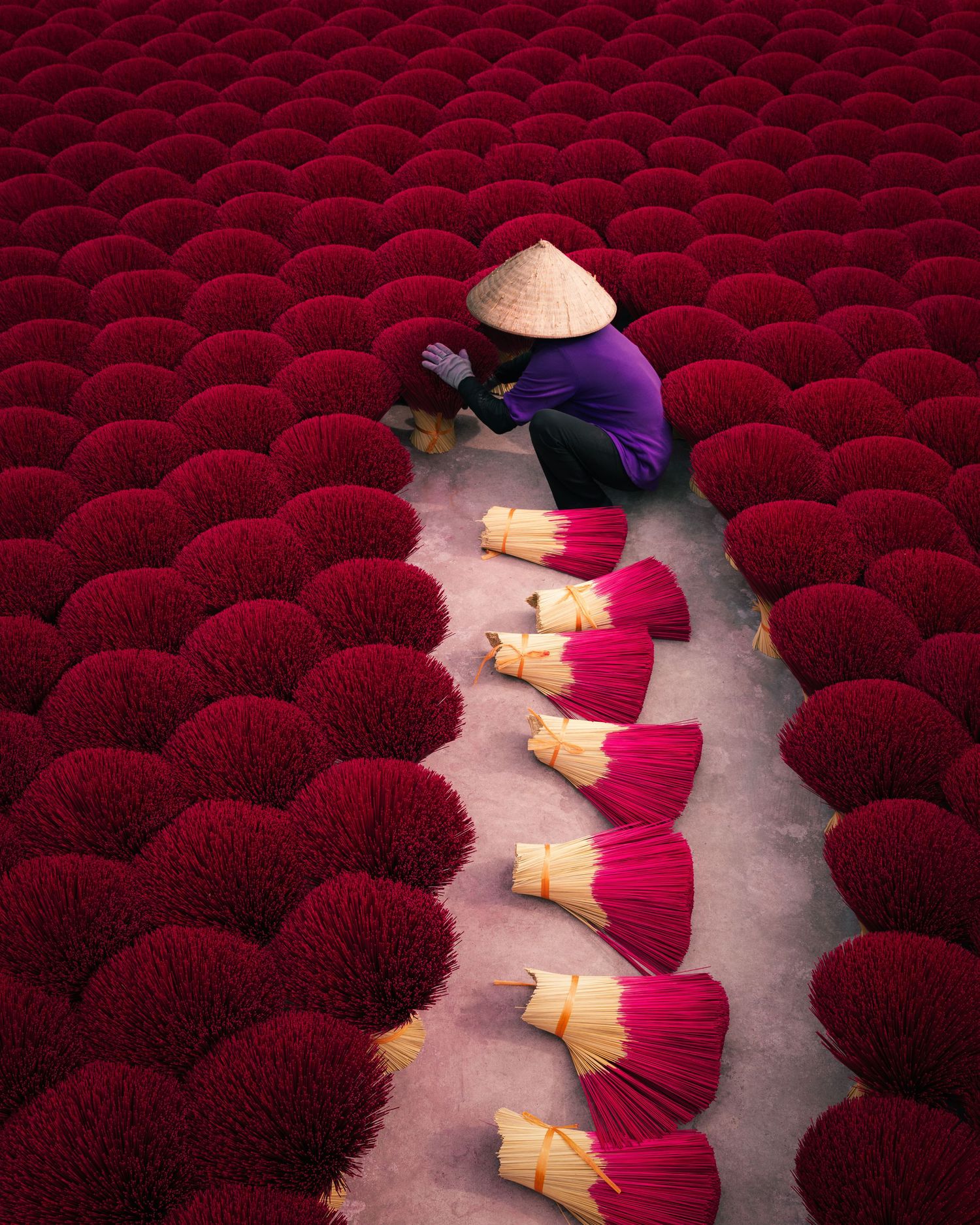 Workers arrange vibrant red incense sticks in neat rows for drying in Vietnam. Photograph by Chris Ha.