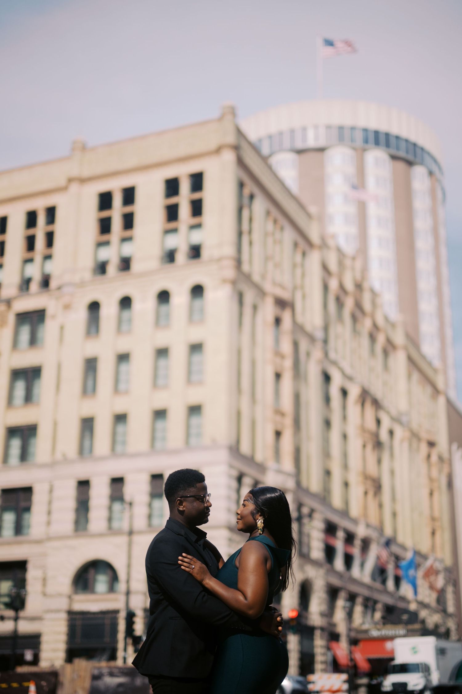 A couple shares an intimate moment outside a historic building with Art Deco architecture in an urban setting.