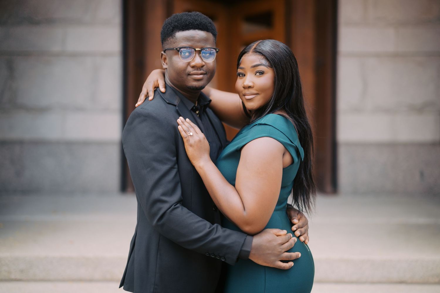 A couple embraces while posing for an outdoor portrait against a stone building entrance.