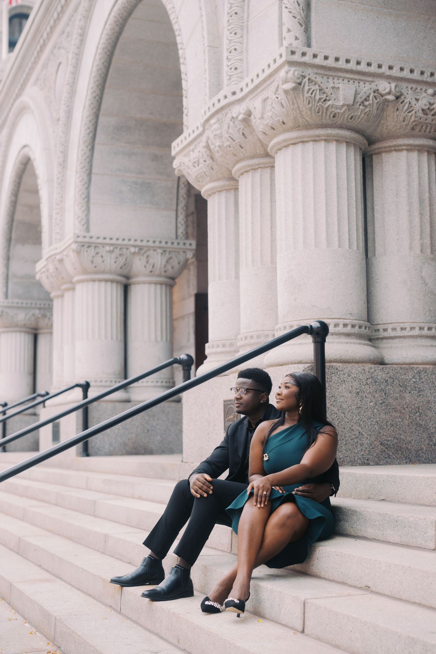 A couple relaxes on elegant white stone steps with ornate architectural columns and arches in the background.