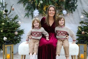 Family poses together in matching winter sweaters against festive holiday backdrop with Christmas trees.