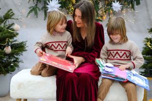 Group enjoying a colorful pop-up book while sitting on white bench with holiday decorations.