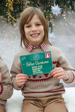 A beige winter sweater with a gingham collar being worn while holding a green letter to Father Christmas during holidays.