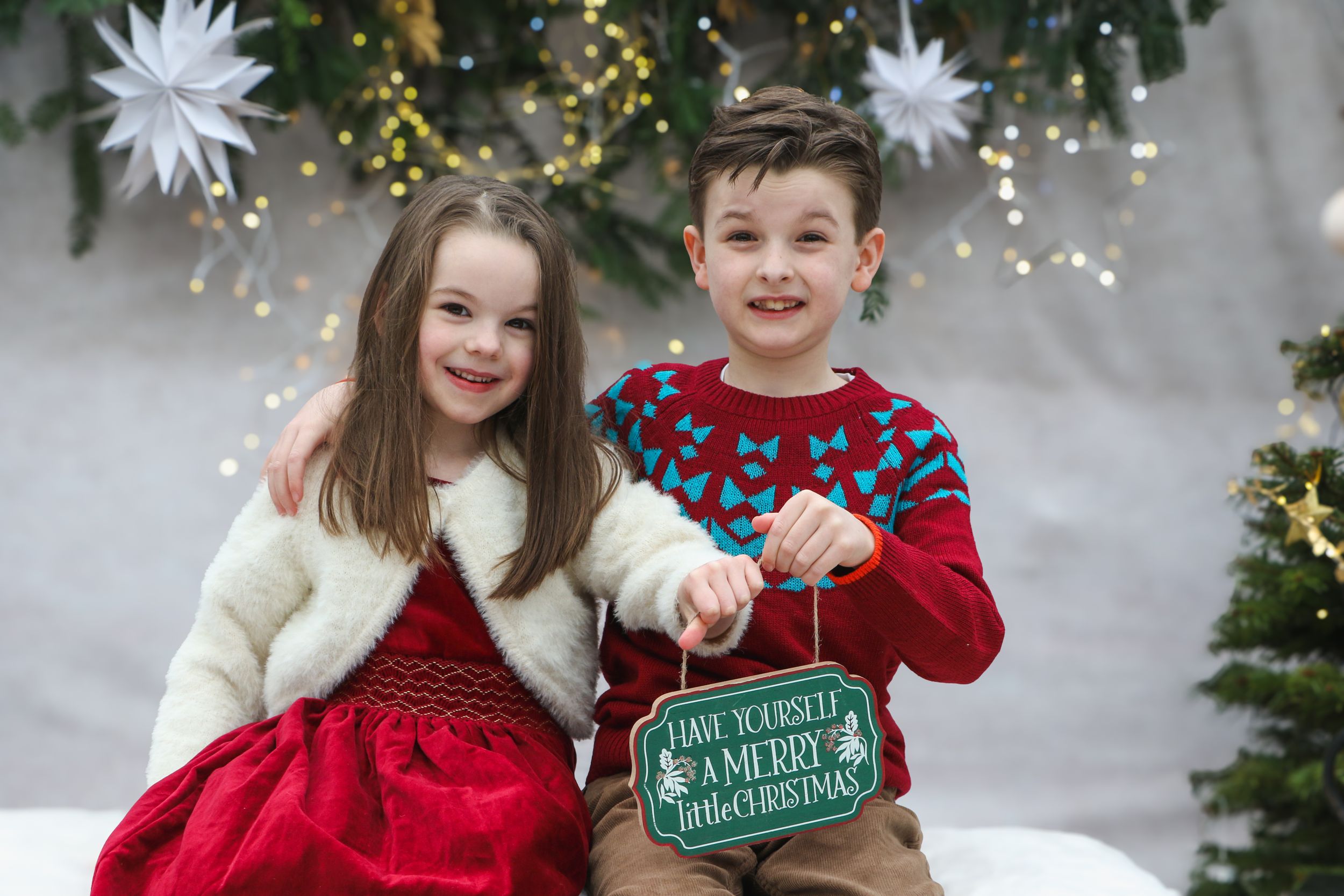 Children sitting together with holiday decorations and holding Santa's Workshop sign.
