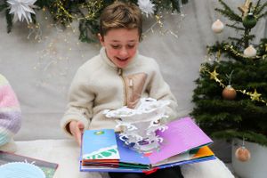 Young child explores a pop-up book near decorated Christmas tree and festive holiday decorations.
