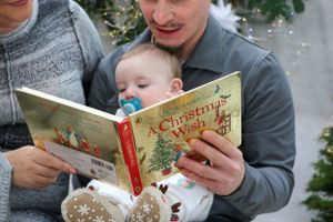 Family reading a Christmas book together with holiday decor in the background.
