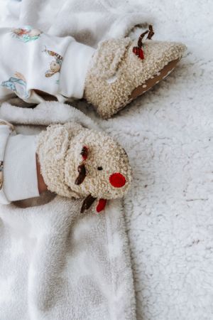 Cozy plush reindeer slippers with white trim and red noses on white fabric.