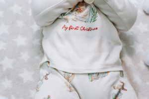White baby clothing with 'My First Christmas' embroidery and festive pattern.