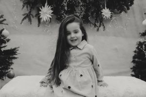 Black and white portrait in front of Christmas decor with evergreen branches and star decorations.