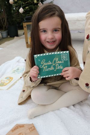 Holiday scene with beige coat showing green North Pole letter near Christmas tree.