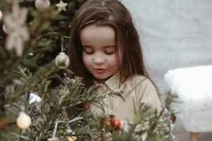Dreamy holiday portrait near decorated Christmas tree with ornaments and lights.