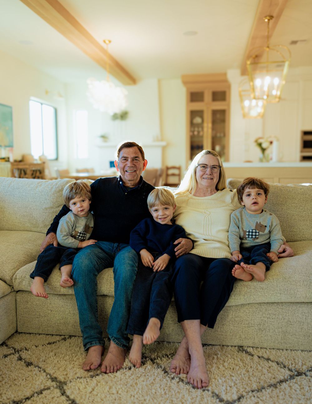 Family relaxing barefoot on a beige couch in a modern living room with wooden beams.