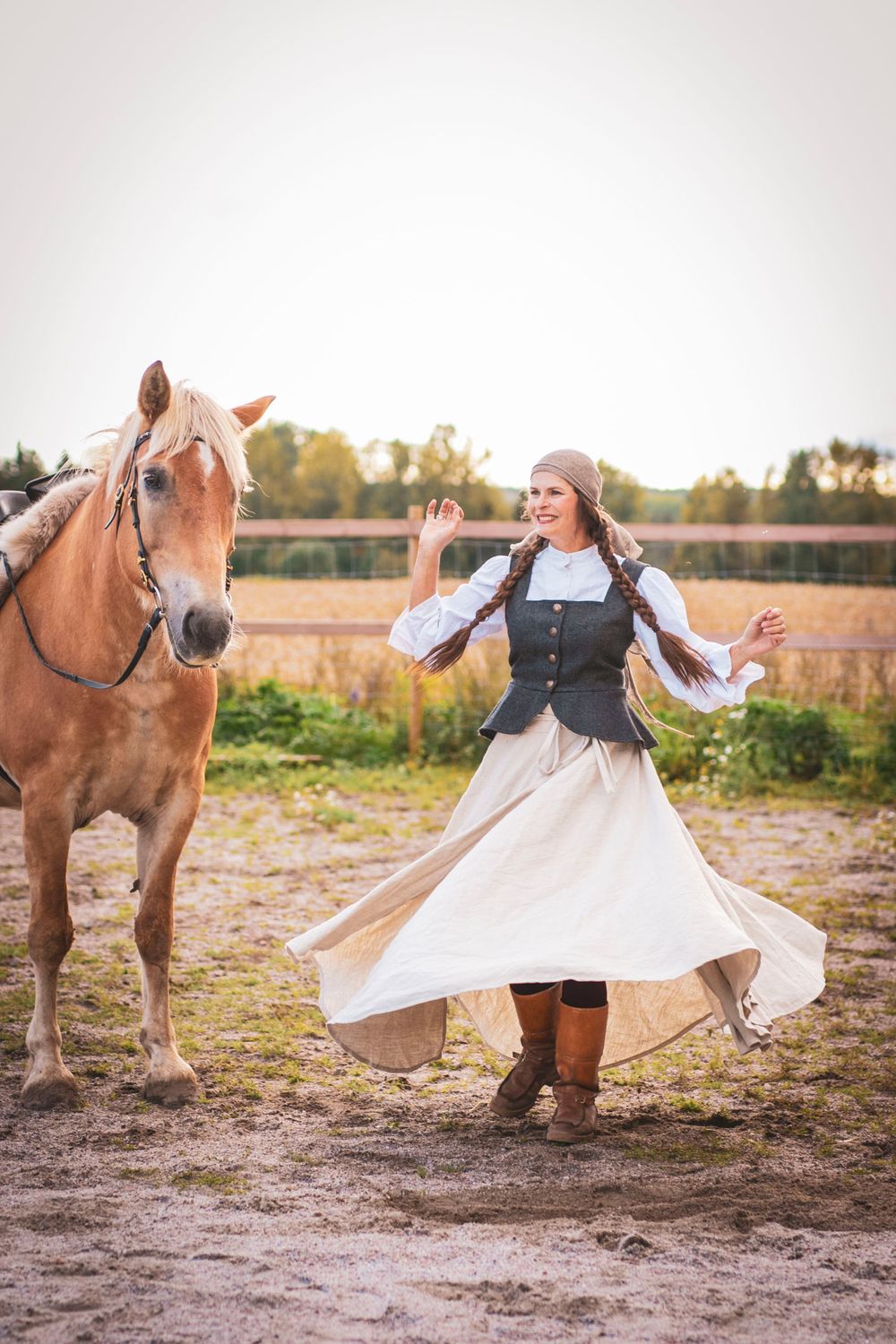 Person in traditional dress dances next to Finnhorse in countryside setting.