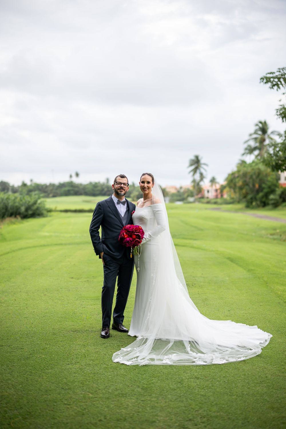 Wedding couple poses on a lush green golf course with tropical palm trees in background.