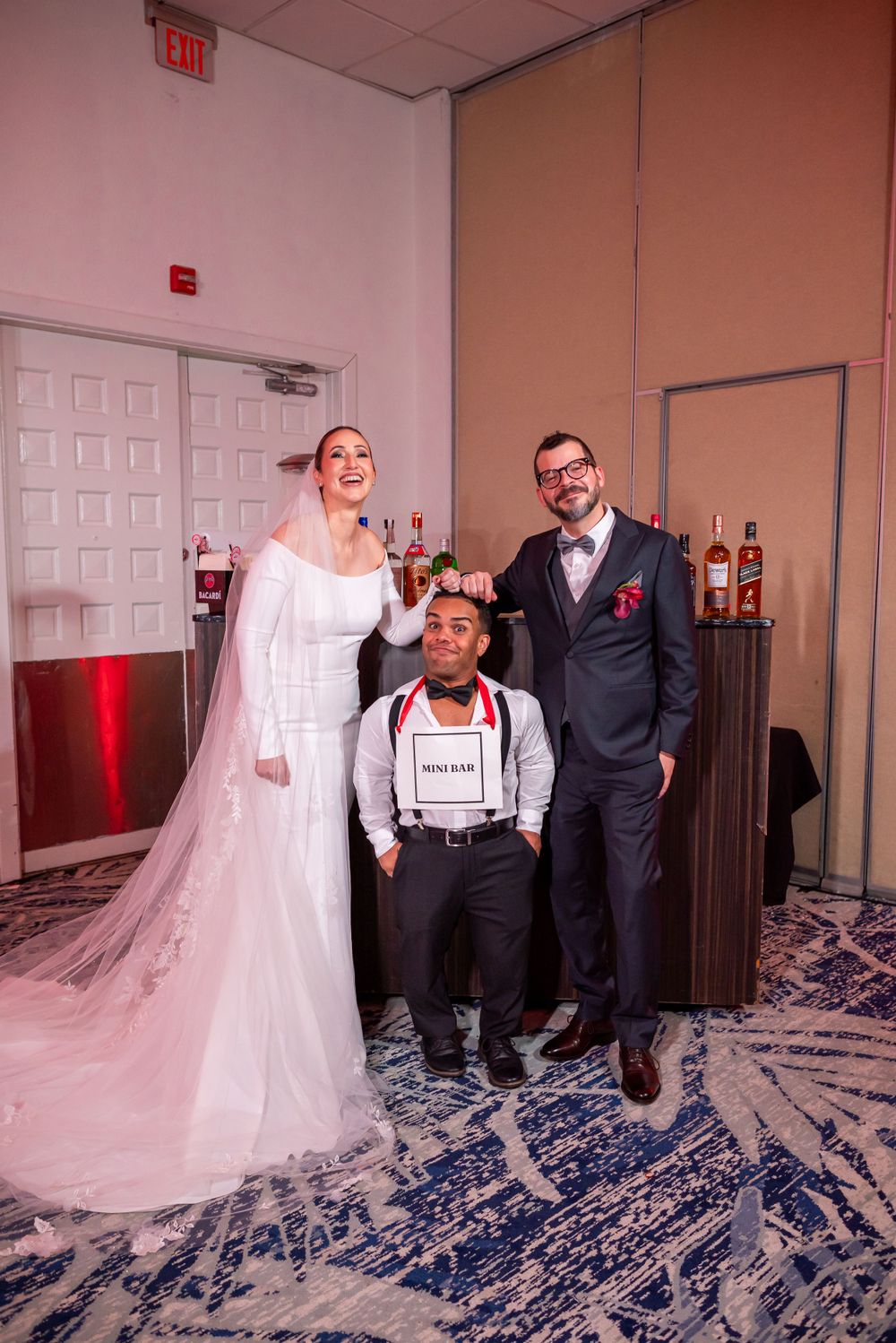 Wedding celebration featuring attendants posing near a bar setup with decorative lighting.