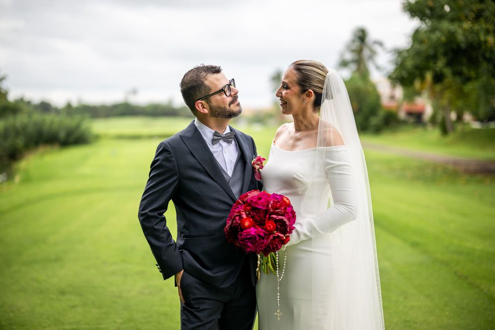 Wedding couple shares a joyful moment on a lush golf course with vibrant red peony bouquet.