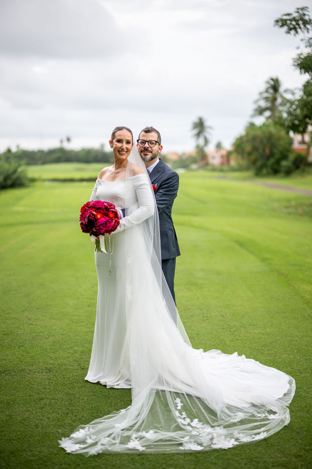 Elegant wedding portrait on a golf course with tropical palm trees and flowing cathedral veil.