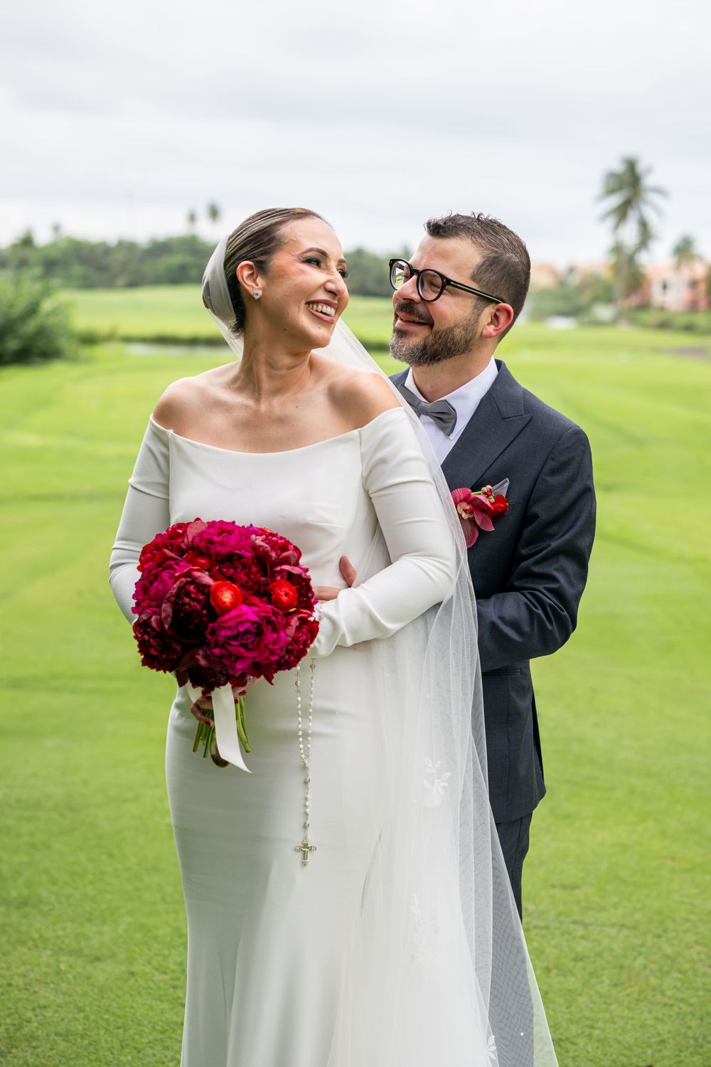 Candid wedding moment captured on a verdant golf course with stunning red bouquet.