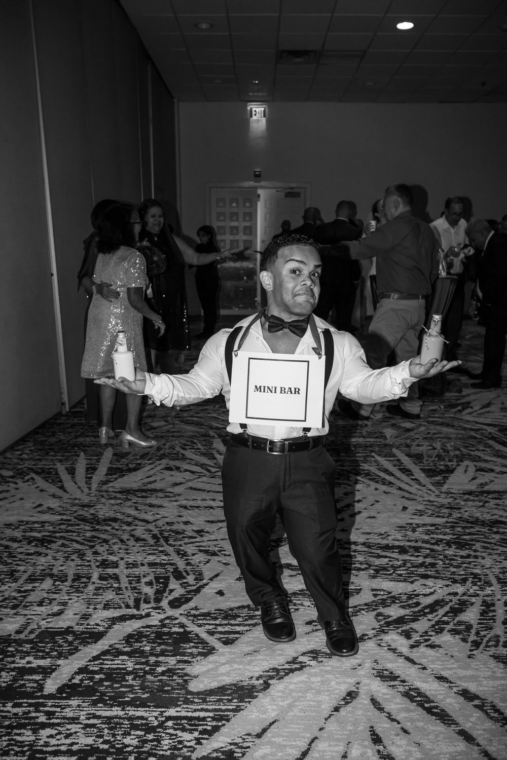 Mini bar attendant in suspenders striking an energetic pose on a patterned carpet at an event.