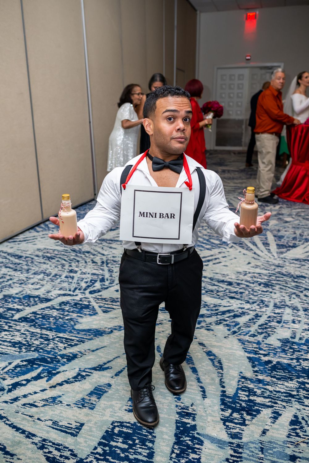 Event staff member wearing a 'Mini Bar' sign performing service duties on blue patterned carpet.