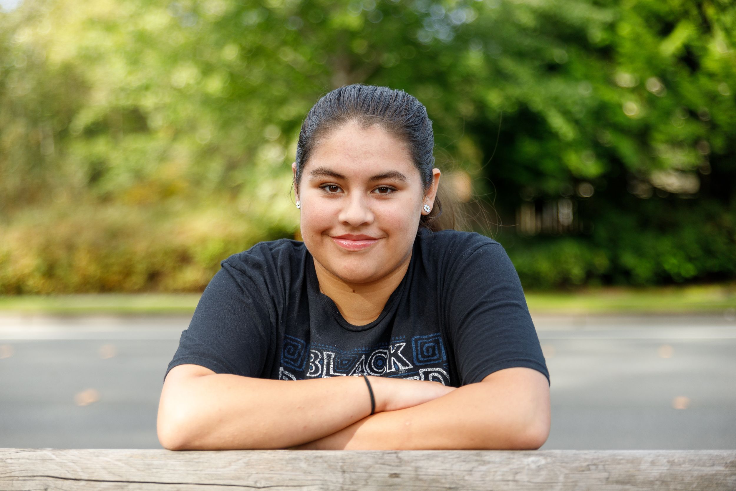 Teen in black t-shirt resting arms on wooden surface outdoors.